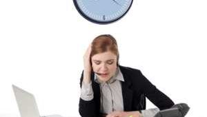 Una mujer trabaja sobre su escritorio y sobre ella cuelga un reloj sobre fondo blanco