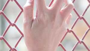 Primer plano de una mano apoyada en una verja de color rojo