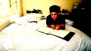 Un chico joven estudia sobre su cama dentro de su ahitaciÃ³n