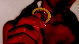 Preservativo en primer termino que sostienen una mujer que se ve desenfocada en segundo plano